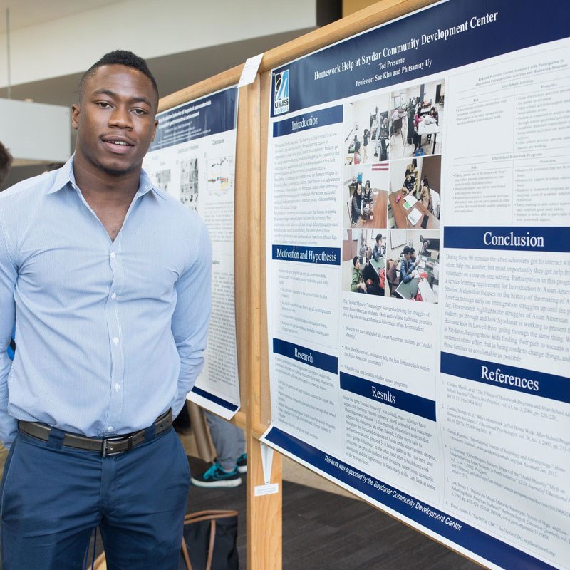 A student stands in front of their research poster.